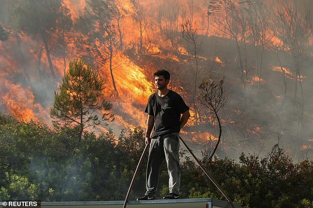 STAMATA -- A volunteer stands on a roof as flames flare from a forest fire raging behind the roof.