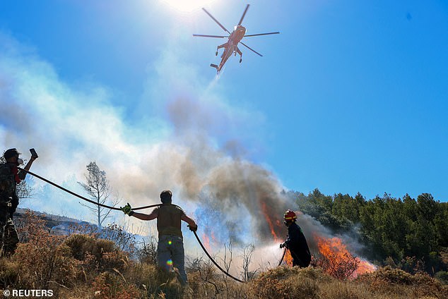 KERATEA -- A firefighting helicopter flies over a firefighter and volunteers trying to extinguish a wildfire, June 30