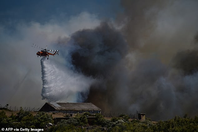 KERATEA -- A helicopter sprays water over a military camp during a forest fire