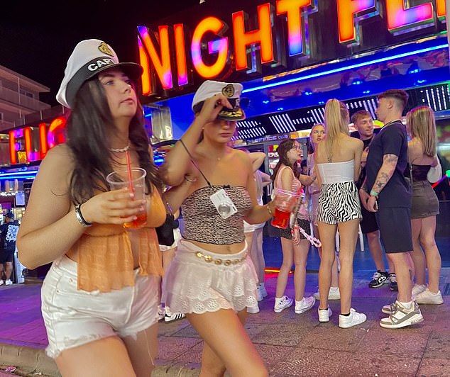 Pictured: Two women wearing 'Captain' party hats walk through the strip
