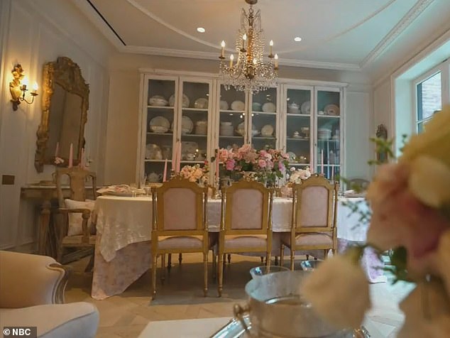 A fabric-covered dining table is flanked by gold chairs, as well as a beautiful chandelier and several bouquets of fresh flowers