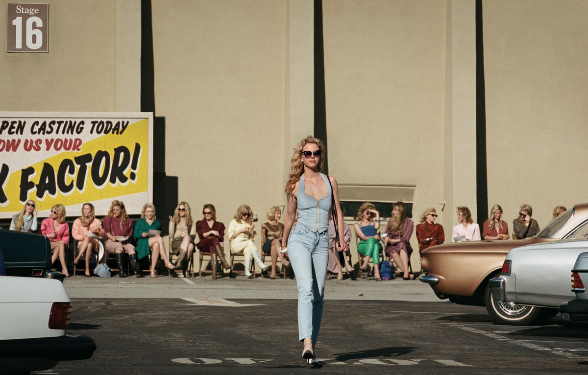 Maxine (Mia Goth) parades through a Hollywood parking lot, outside a movie studio, with a line of other auditionees sitting in chairs behind her, in Maxxxine 