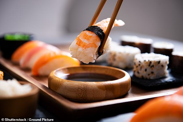 Pictured: A photo of a guest holding bamboo chopsticks with nigiri shrimp while soaking them in soy sauce