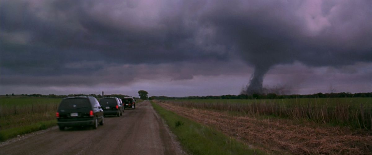 Three vans drive down a country road, while in the distance a large tornado is visible in Twistter.