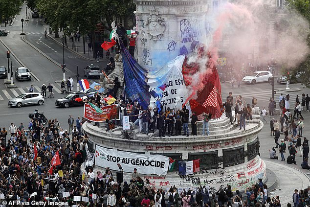 Crowds of people hold up a giant national flag with the text 