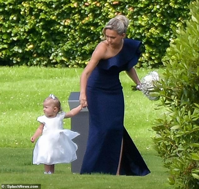 The former Love Island star, 24, wore a navy off-the-shoulder dress as she entered the ceremony hand-in-hand with her 18-month-old little one, who wore a cute white dress