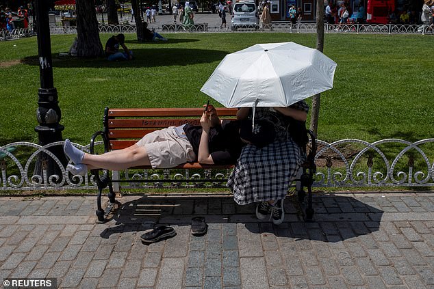 People seek shelter from the sun with an umbrella as they stand still in Sultanahmet Square, one of the city's most famous tourist attractions, in Istanbul, Turkey, June 28, 2024