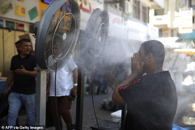 A man cools down as he stands in front of 'water sprinklers' placed along the side of the road as temperatures rise in the capital Baghdad on June 30, 2024