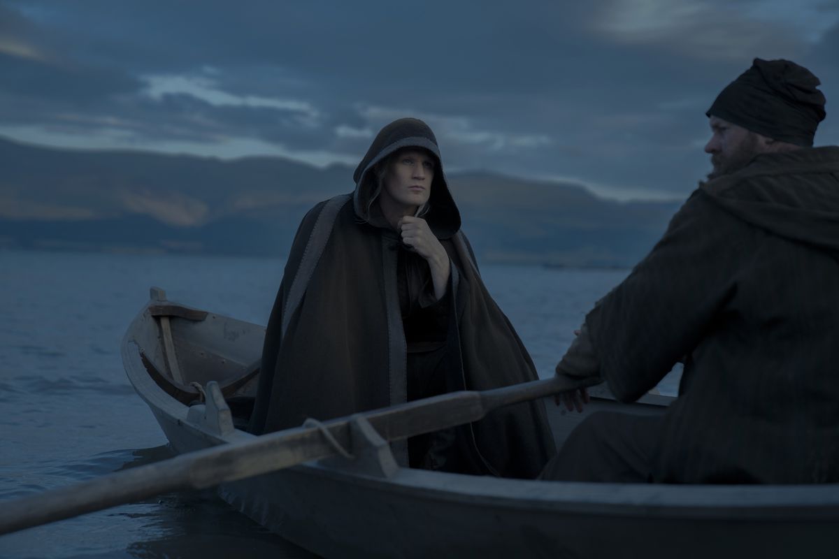 Matt Smith as Daemon Targaryen, wearing a large hooded cloak and riding in a small boat in House of the Dragon