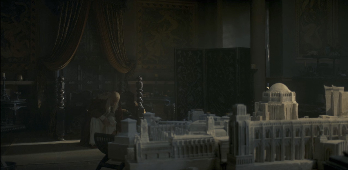 King Viserys (Paddy Considine) sitting in his room, with his King's Landing model in front of him. You can see sex frescoes in the background behind him on his bedroom wall