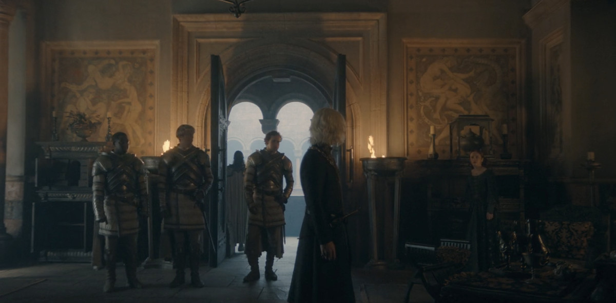 Aegon (Tom Glynn-Carney) stands and looks at his mother (Olivia Cooke). Behind her you can see a wall with some human/dragon sex tapestries.