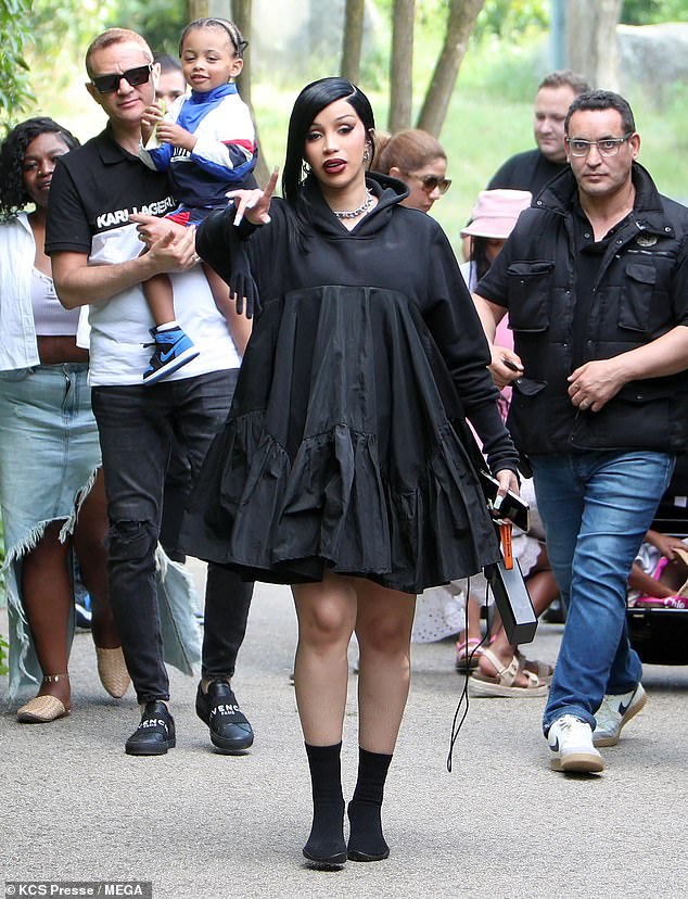 Cardi looked glamorous for the outdoor occasion in an oversized black hooded dress and boots