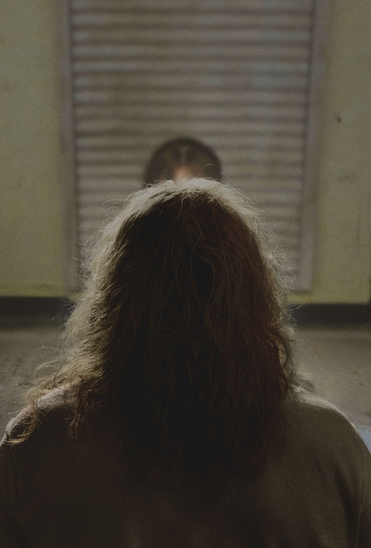 The back of Nicolas Cage's head in Longlegs, as he sits at a metal table in an interrogation room 