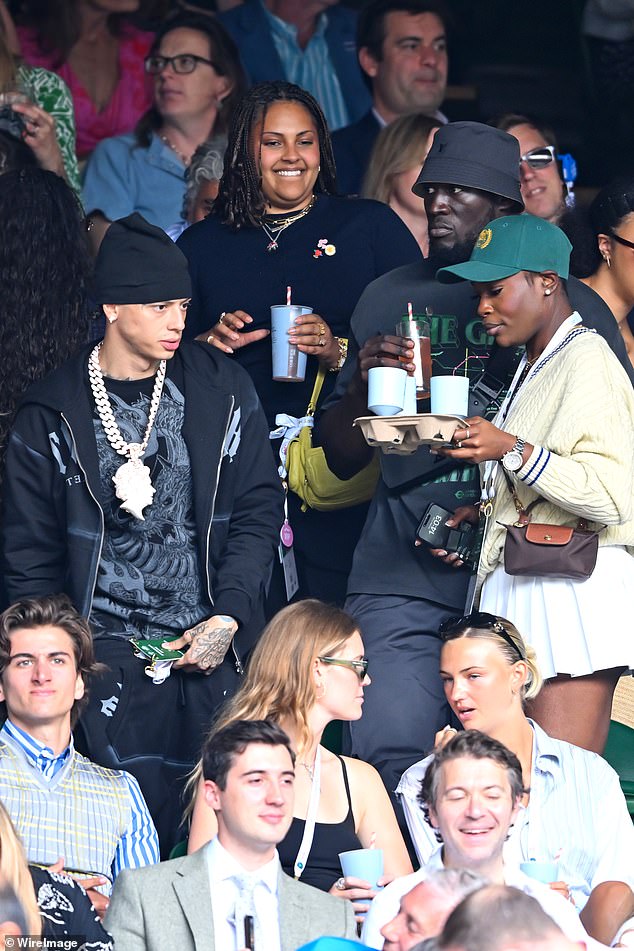 Carrying his drink to his seat as he prepared to watch all the tennis action, the white Central Cee wore a necklace with the Queen on it