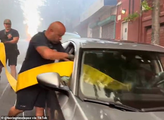 Once both windows are clean, one of the firefighters quickly throws away the bags of trash lying around the fire hydrant before helping his colleague grab the bright yellow hose