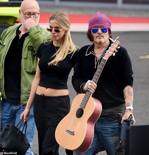 The unknown companion matched his style, wearing an all-black casual yet chic outfit, baring her stomach and holding a handbag, accessorizing with rectangular-framed sunglasses.