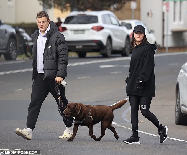 The former Rabbitoh held his phone and bottle, as well as the leash of Danika's chocolate Labrador Charlie as they walked