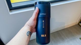 A hand holding the Ember Travel Mug 2+ with the LED display cover