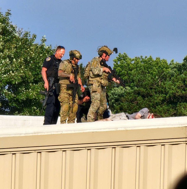 Police stand over the gunman's body on a building across from the rally site