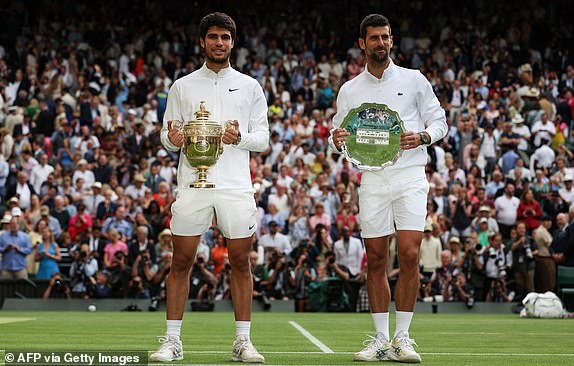 TOPSHOT - Spaniard Carlos Alcaraz (L) holds the winner's trophy as he poses with Serbia's Novak Djokovic after their men's singles final on the final day of the 2023 Wimbledon Championships at The All England Tennis Club in Wimbledon, south-west London, on July 16, 2023. (Photo by Adrian DENNIS/AFP) / RESTRICTED TO EDITORIAL USE (Photo by ADRIAN DENNIS/AFP via Getty Images)