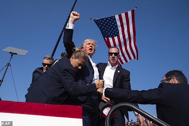 Trump raises his fist to the crowd as he is pushed off the stage by security after being shot