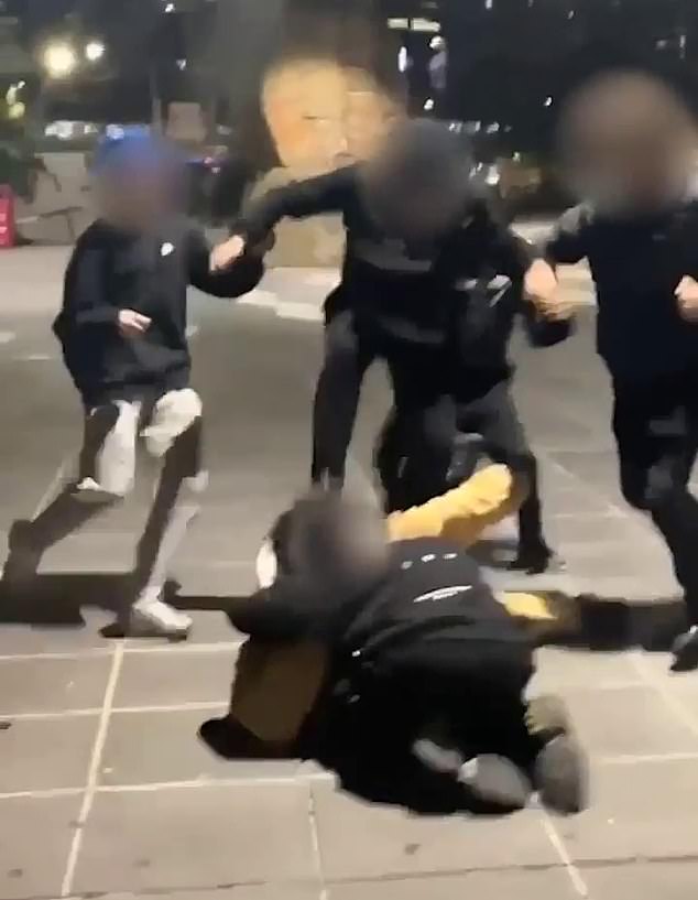 At least five teenagers pushed the food delivery man to the ground and then kicked and punched him in the head (the teenagers in black can be seen stomping on the man in the photo)