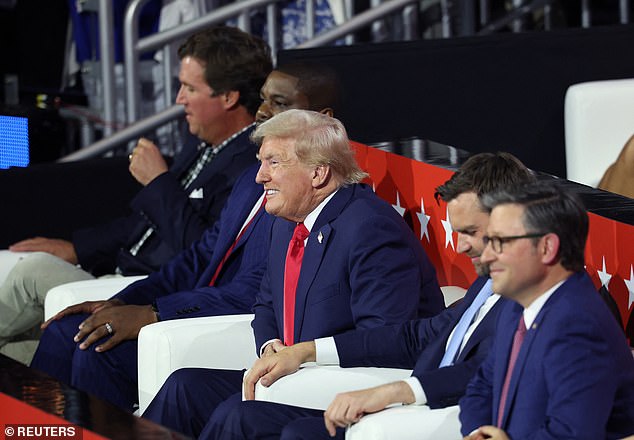 Former President Donald Trump grins from his friends and family box Monday night at the Republican National Convention, flanked by Tucker Carlson, Rep. Byron Donaldson, Sen. J.D. Vance and House Speaker Mike Johnson