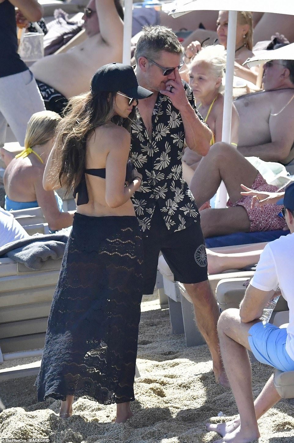 Matt wore a black and beige shirt as he chatted with friends on the sandy beach with his wife