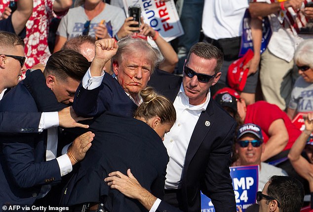 Donald Trump clenches his fist after being shot as his Secret Service escorts him away from the stage during his rally in Butler, PA on Saturday