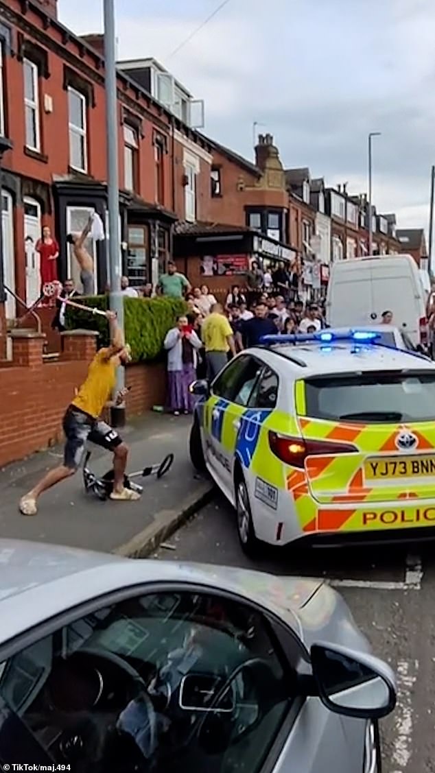 A man uses a scooter to vandalize a police car as people watch and film on their cell phones