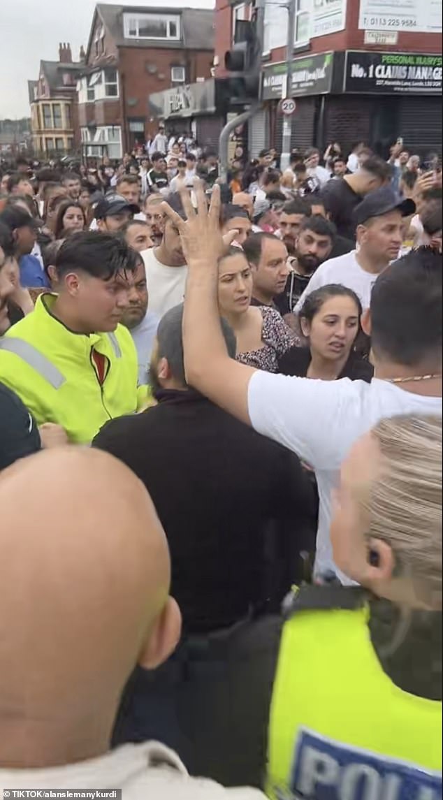 Police officers try to control the crowd that has gathered at the address