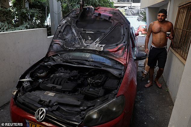 A Tel Aviv man stands next to a damaged car near the site of the deadly explosion amid the Israel-Hamas conflict in Tel Aviv