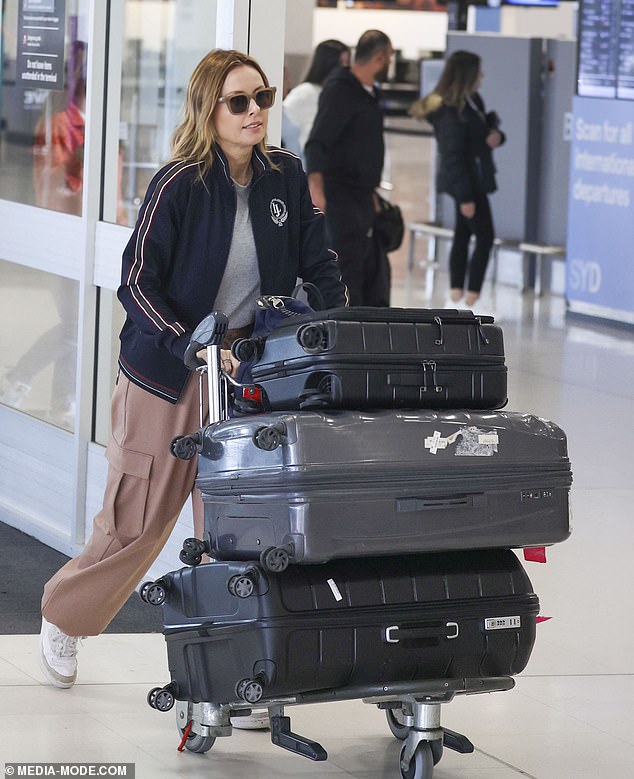 She completed her look with tan pants and white sneakers, accented with stylish sunglasses, and looked focused as she wheeled her luggage through the busy terminal