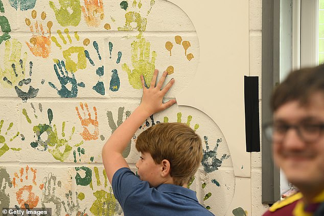 George smears blue paint over his hand and presses it against a wall to leave a handprint at the Big Help Out in Slough