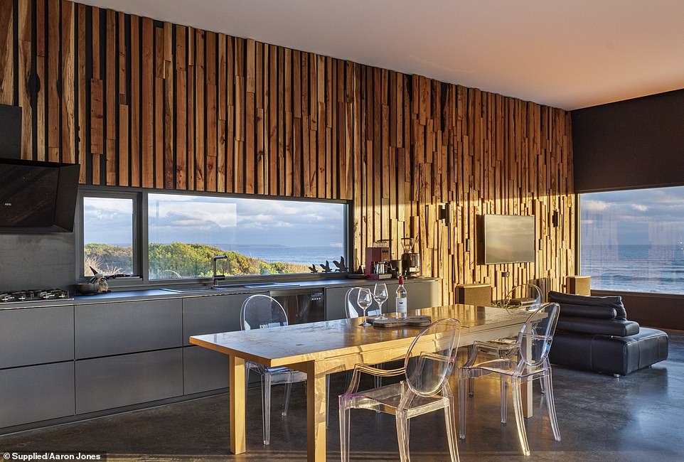 The spacious modern kitchen with sleek concrete floor is finished with black and stainless steel elements and offers a captivating view of the ocean