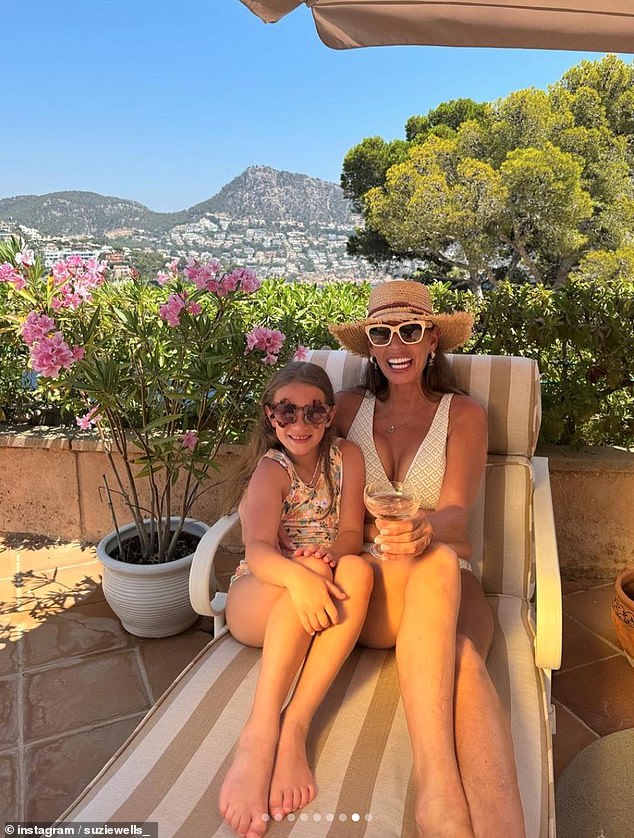 In another photo, Suzie is seen in a tight white swimsuit as she poses with her granddaughter - a drink in her hand