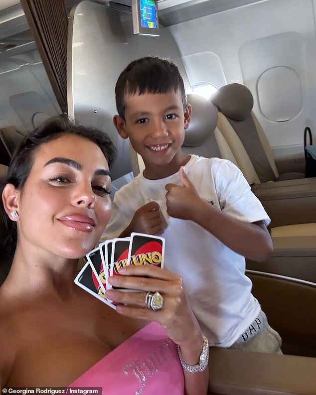 Georgina beamed in the strapless crop top as she took a selfie with her son as they played card game Uno on the plane