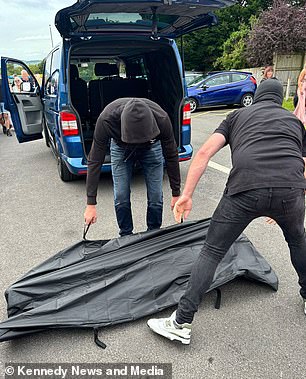 Men in balaclavas prepare to unzip one of the bags