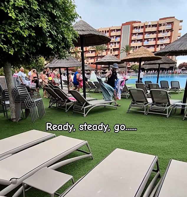 A man in a bucket hat, pictured in the center, throws towels over a row of three beds before moving to another set of three