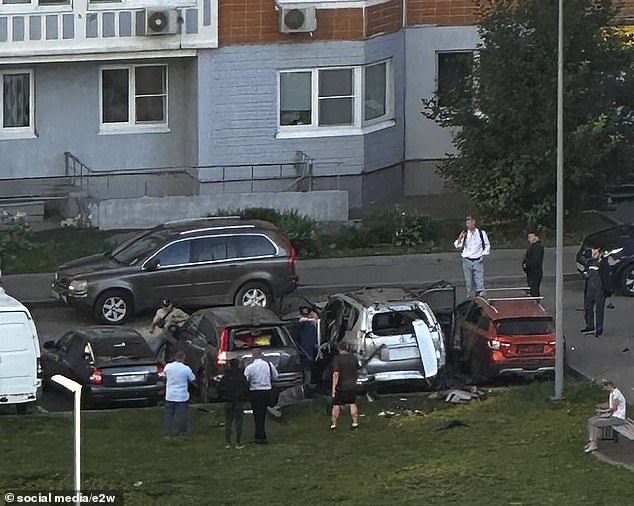 Community members stand around the car explosion that occurred on Sinyavinskaya Street in northern Moscow