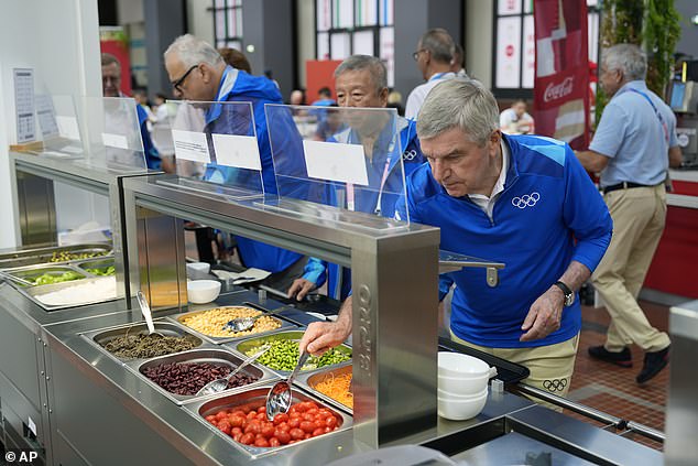 IOC President Thomas Bach tries food from a salad bar during a tour of the Olympic Village in preparation for the 2024 Summer Olympics on Monday