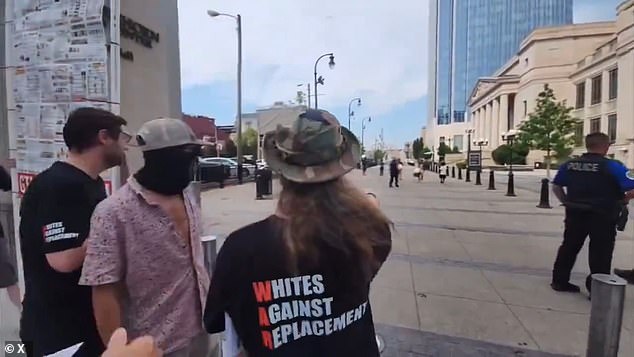 The men wear T-shirts that read “Whites Against Replacement,” while one man wears a face covering with a swastika on it.