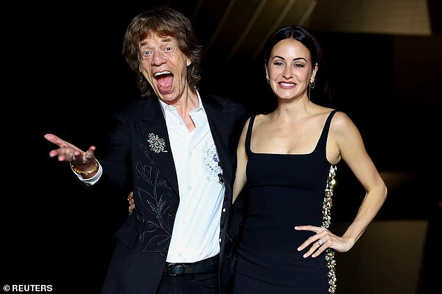 Mick's pants were tight and he put an arm around Melanie, who was wearing a sleeveless black dress with gold trim