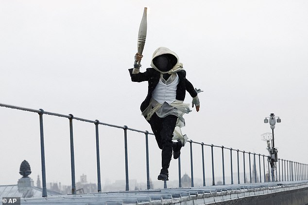 A masked torchbearer runs across the roof of the Musée d'Orsay in Paris, France, during the opening ceremony