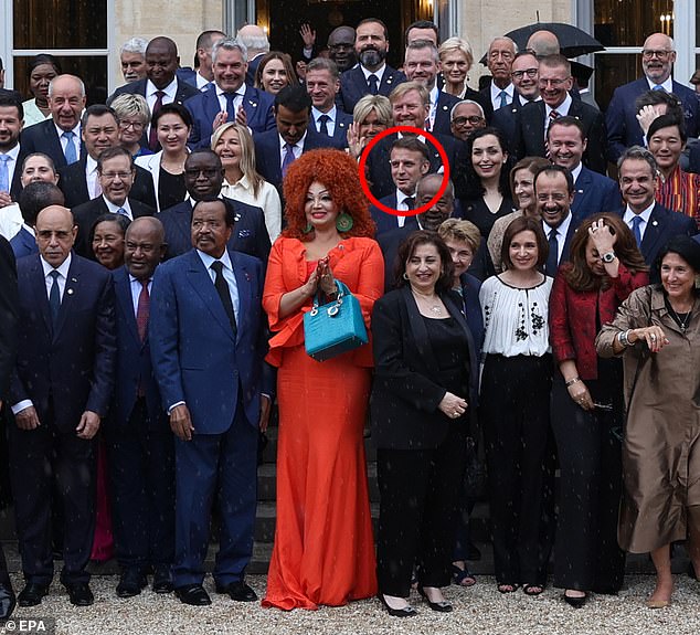 The striking ensemble makes it almost impossible to spot Macron standing right behind her