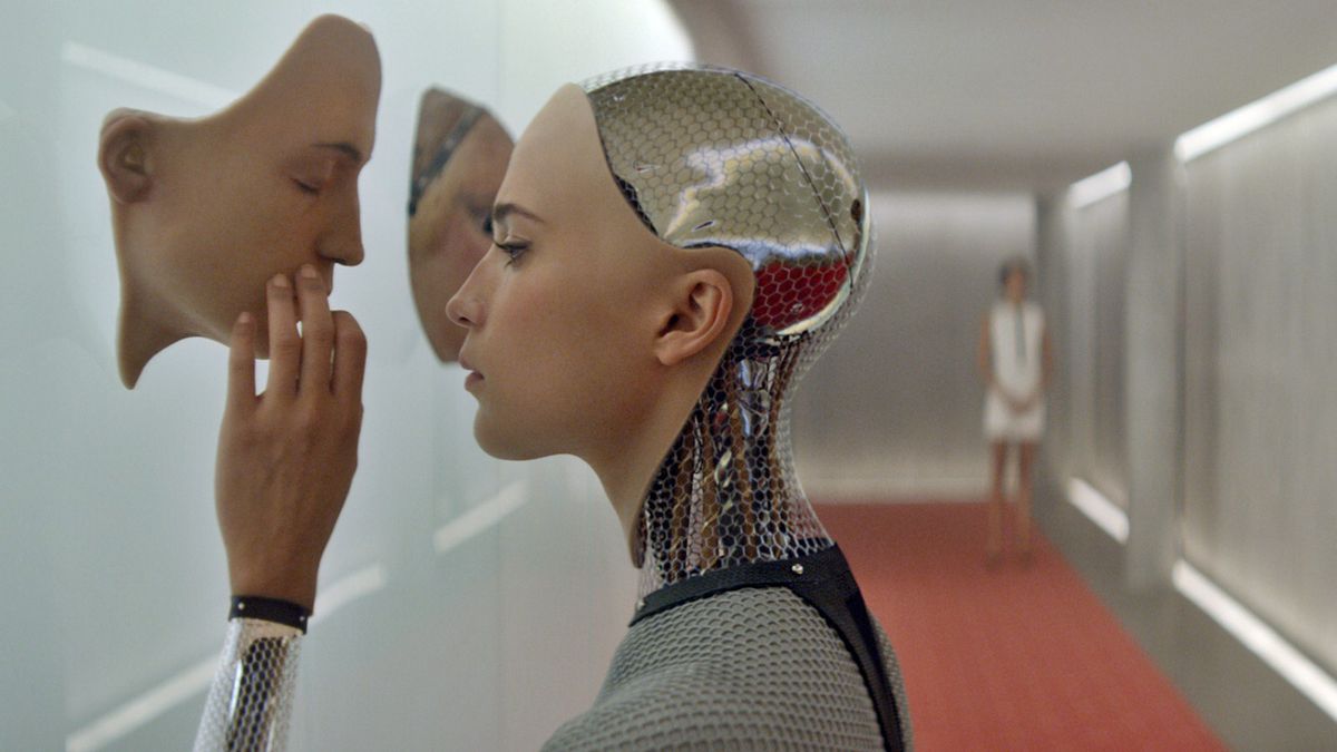 An android woman touches an artificial face hanging on a wall, while a woman in a white dress stands at the end of a futuristic-looking hallway lined with faded red carpet.