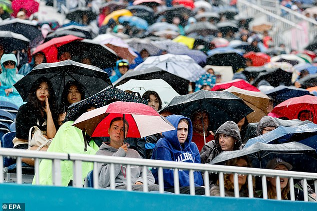 Spectators use umbrellas and raincoats to protect themselves from the rain during the opening ceremony