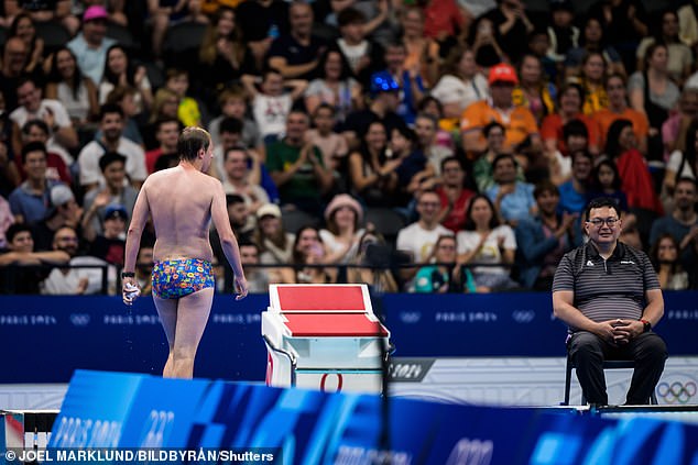 Fans in the background applaud as the man leaves the Olympic pool