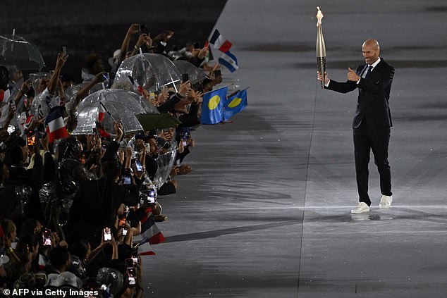 Former French footballer Zinedine Zidane carries the Olympic flame past athletes