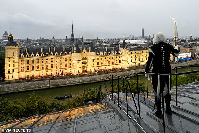 A torchbearer carries the Olympic flame over a building along the Seine during the opening ceremony